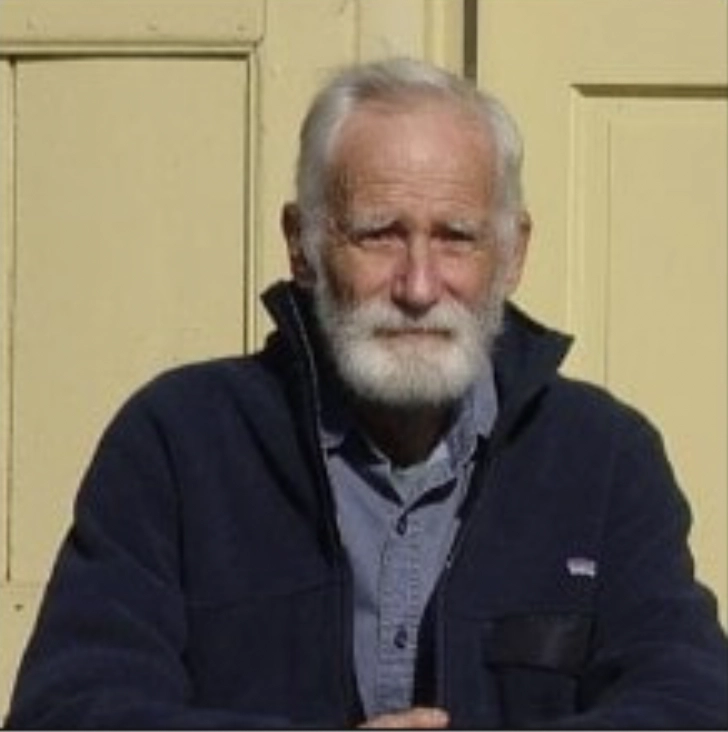 A portrait of an elderly man with white hair and a beard, wearing a blue zip-up fleece.