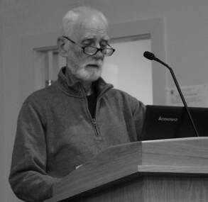 Older man with glasses speaks at a podium with a microphone and a laptop.